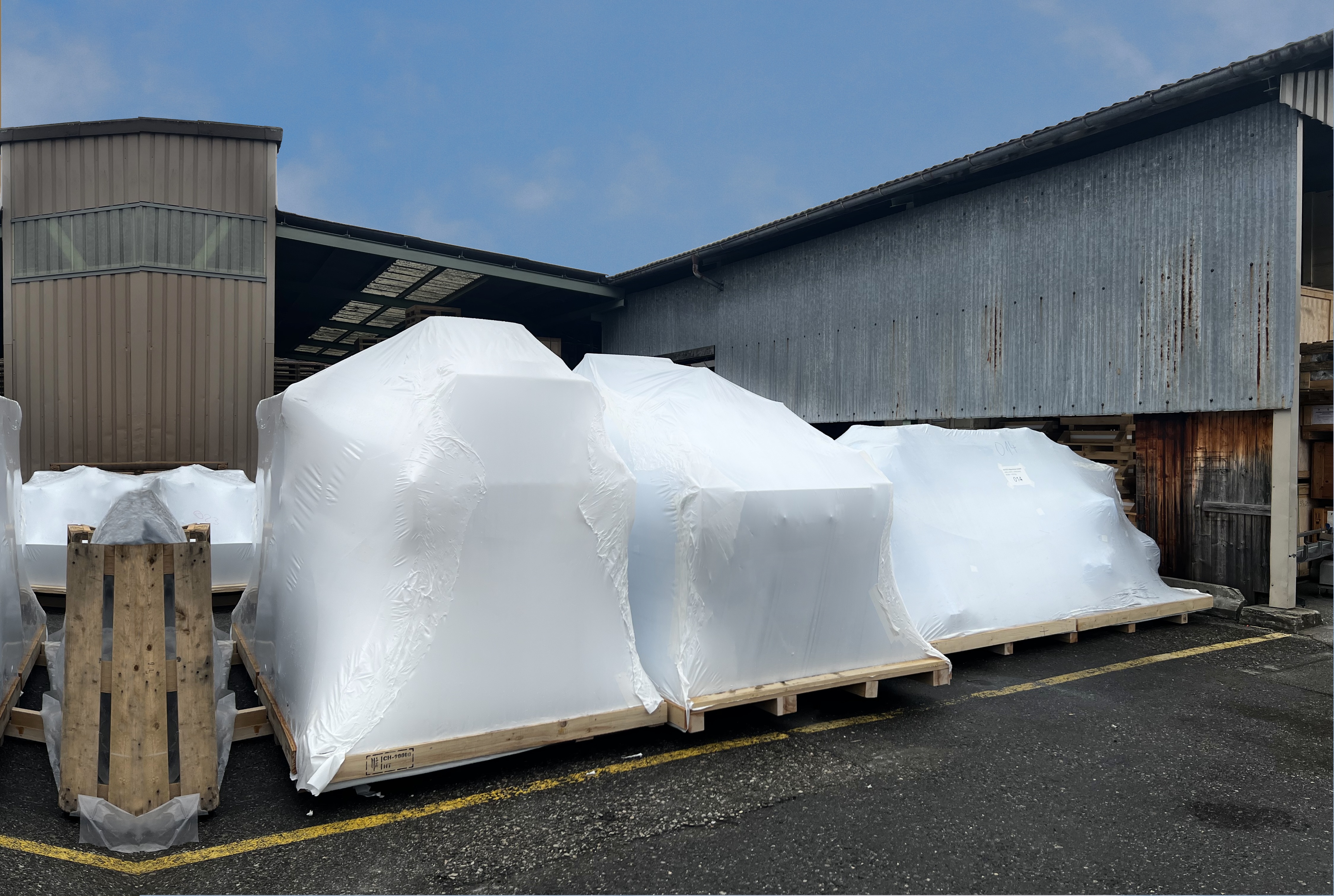 Auf einem Transportboden festgetackerte, weisse Schrumpfverpackung schützt das Packgut draussen vor dem Wetter.