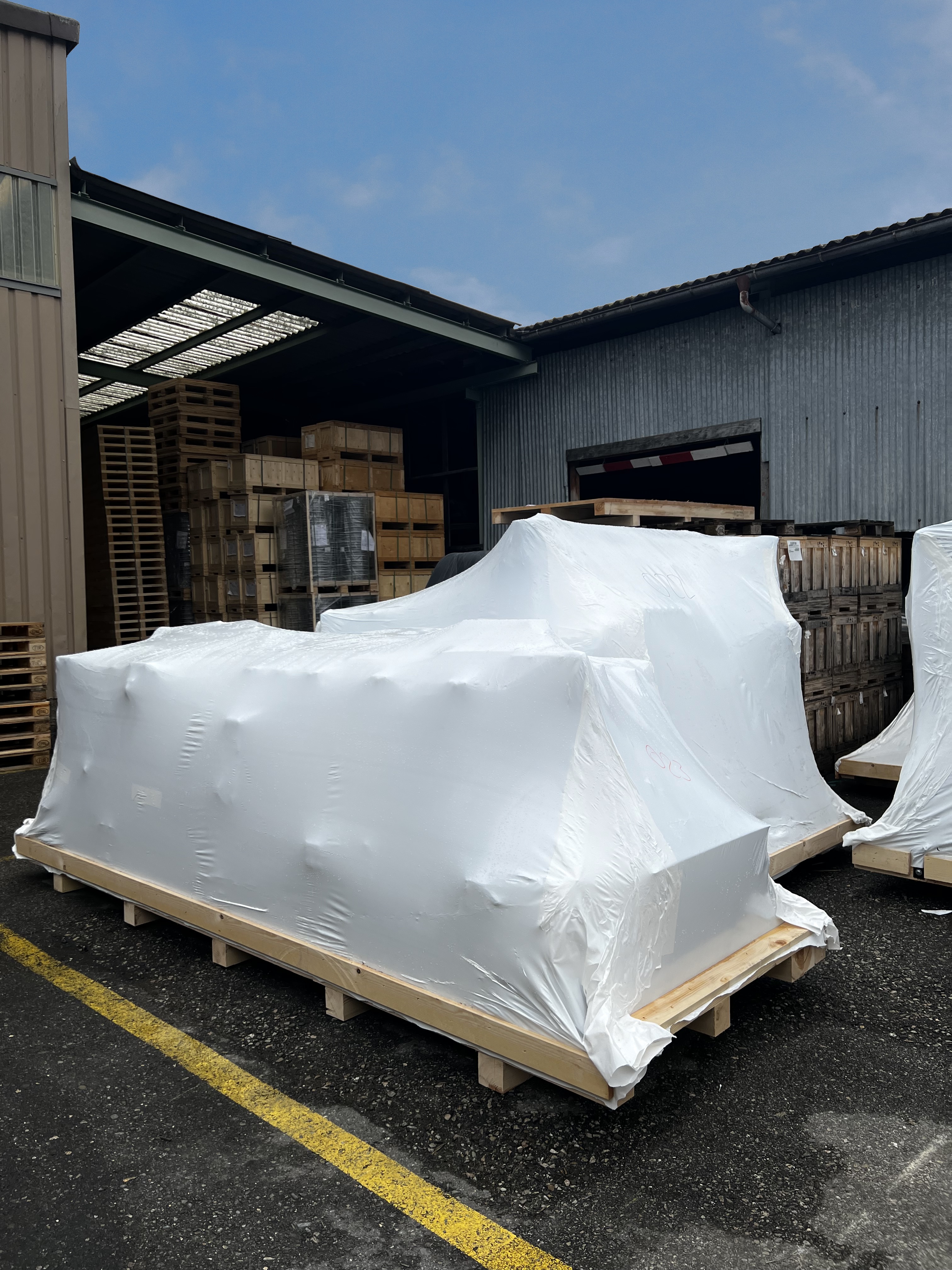 Auf einem Transportboden festgetackerte, weisse Schrumpfverpackung schützt das Packgut draussen vor dem Wetter.