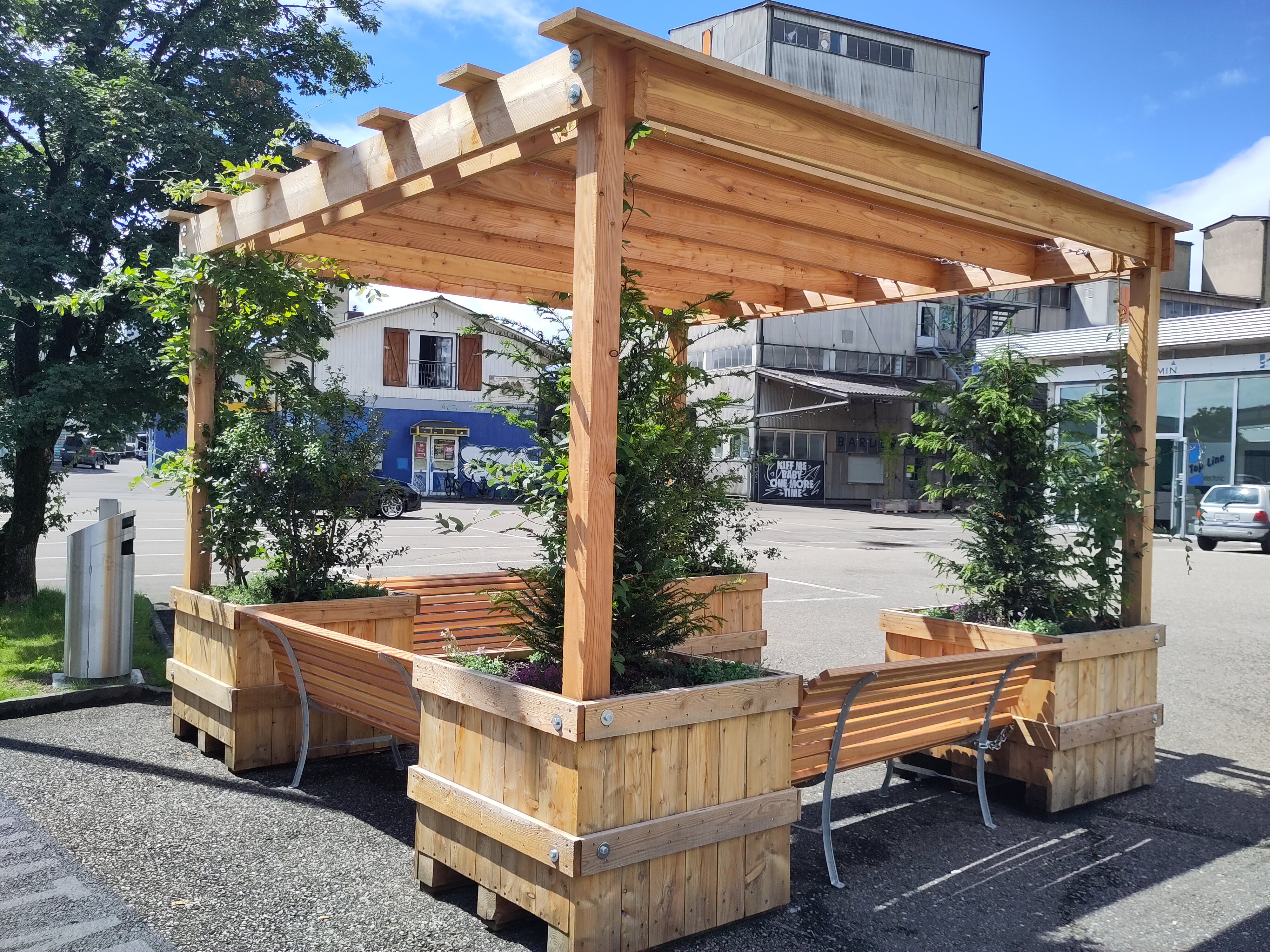 Die Spezialanfertigung aus Holz beinhaltet vier grosse Blumenkästen mit einer Pergola und drei Sitzbänken.